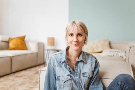 Smiling Middle-Aged Blonde Woman Sitting on Living Room Floor