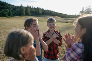 Portrait of young classmate playing hand clapping game outdoors. Students during field teaching class, standing in the middle of meadow, having fun.