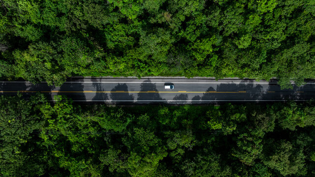 Aerial view electric vehicle car or EV car on green forest road, EV car travel in green season, Asphalt road and green forest, Forest road going through forest with electric car. - Powered by Adobe