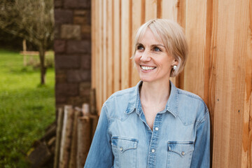 Smiling Woman in Denim Shirt Leaning Against Wooden Wall