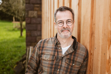 Smiling Senior Man Leaning Against a Wooden Wall Outdoors
