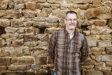 Mature Man with Glasses Smiling Outdoors against Stone Wall - 791412833