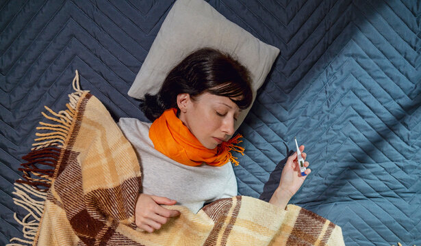 Woman holding thermometer and taking nap on bed at home
