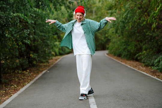 Happy young woman listening to music through wireless headphones and dancing on road