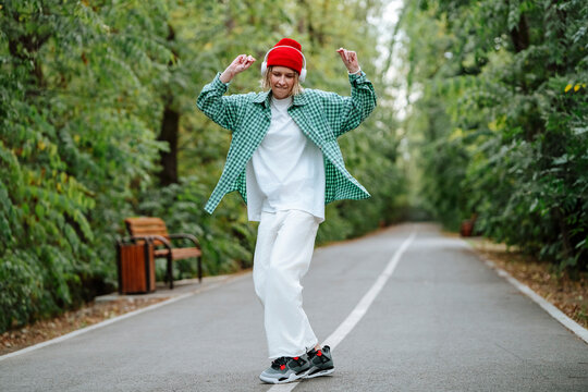 Happy woman wearing wireless headphones and dancing on road near trees