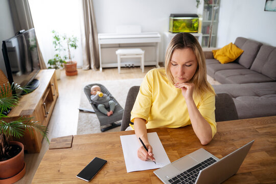 Businesswoman writing on paper at table with son in background
