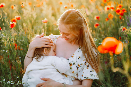 Smiling mother breastfeeding daughter in flower field