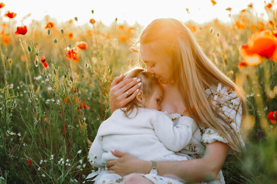 Mother kissing daughter and breastfeeding in flower field