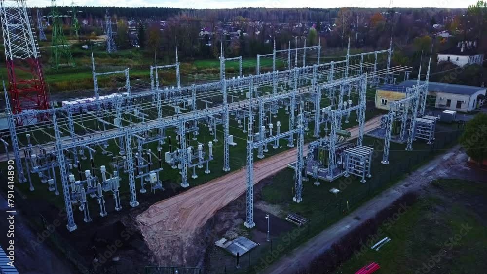 Poster tilting drone shot over a high-voltage distribution site on the edge of a village.
