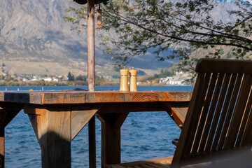 A wooden table with two salt and pepper shakers sits on it overlooking a lake at a waterfront cafe or restaurant. The concept of a cozy atmosphere, offering a place to unwind, relax, and enjoy nature