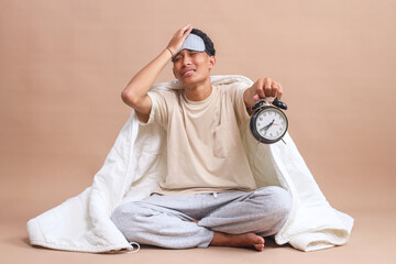 Panic Young Asian Man in Pajama Holds Alarm Clock Wake Up Late Isolated on Beige Background