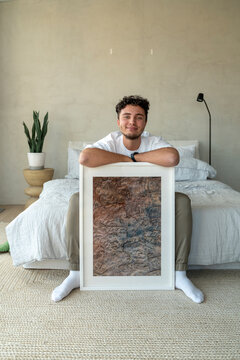 Smiling young man sitting with picture frame on bed at home
