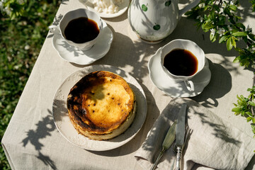 Plate of cheese cake and cups with coffee served on tablecloth. Beautiful outdoor breakfast