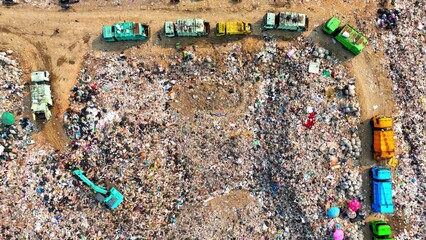 The sprawling expanse of a landfill: a grim tableau of waste heaps, dirt trails marked by trucks,...