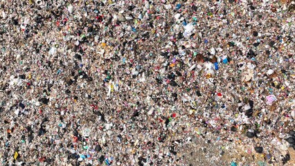 A tightly packed expanse of trash, depicting a variety of discarded items creating a multicolored, textured surface. Garbage background. Aerial view.
