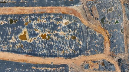 Hovering in the sky, the landfill veiled in swathes of black plastic underscores our environmental imprint and containment initiatives. Landfill background. Aerial view.
