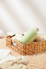 Bathroom background from front view with some baby bath products, rectangle rattan basket containing a unlabeled green bottle and a few necessities on white texture. Space for design
