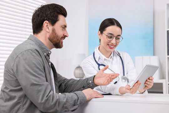 Doctor with tablet consulting patient during appointment in clinic
