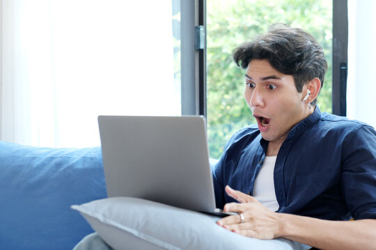 Young man surprising while looking at laptop computer, work at home