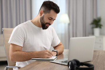 Young man writing down notes during webinar at table in room