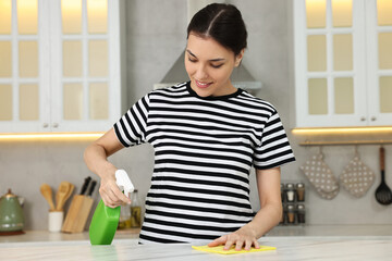 Woman cleaning countertop with sponge wipe and spray bottle in kitchen