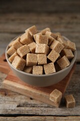 Brown sugar cubes in bowl on wooden table, closeup