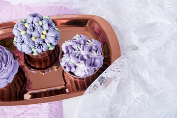Top view of aesthetics purple floral cupcakes with cup of coffee. No sugar dessert among lilac flowers.