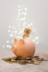 Piggy bank with euro banknote and coins on grey table against blurred lights, space for text
