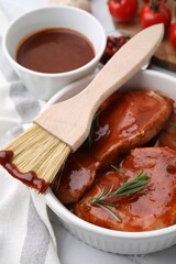 Raw marinated meat, rosemary and basting brush on table, closeup