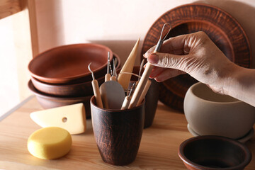 Woman taking clay crafting tool from cup in workshop, closeup