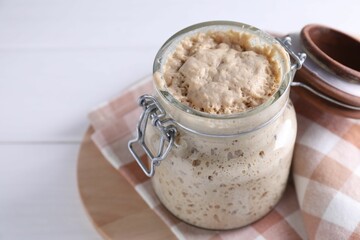 Sourdough starter in glass jar on white table, closeup. Space for text