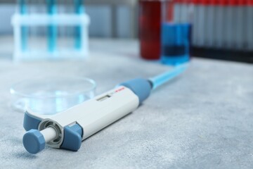 Laboratory analysis. Micropipette with liquid and petri dish on light grey table, closeup. Space...