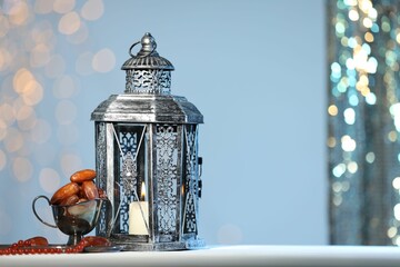 Arabic lantern, misbaha and dates on table against blurred lights, space for text