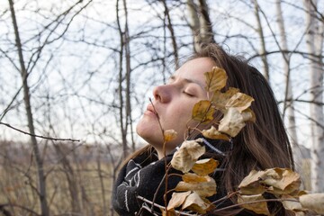 Thoughtful young woman standing in the autumn forest with closed eyes