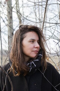 Thoughtful Woman in Black Coat and Geometric Scarf in Front of Bare Tree Branches