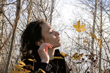 Woman standing peacefully in autumn forest, eyes closed, surrounded by falling leaves. - 791434625