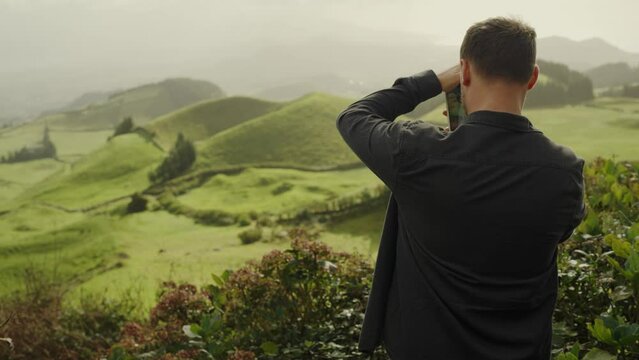 Back view on male tourist take picture of green hills outdoors using smartphone camera. Man shooting beautiful nature landscape with valley on mobile phone