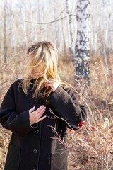 Stylish Woman in Black Coat Standing Thoughtfully in Serene Forest with Sunlight Through Trees - 791436024