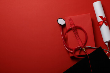Graduate hat with diploma and stethoscope, on red background.
