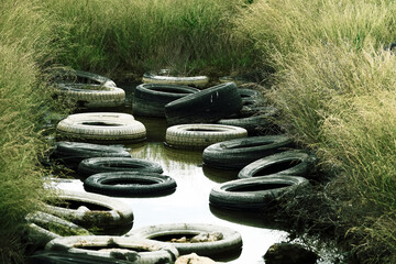 The reservoir is littered with car tires. Pollution of the environment by cars and waste around the...