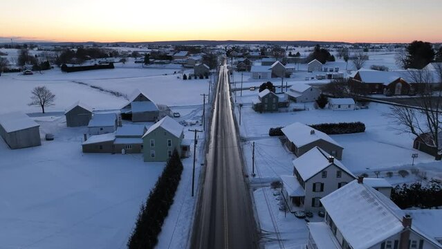 American countryside during winter sunrise with snow covered landscape. Aerial over rural country road.