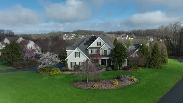 Two-story American suburban home with green lawn and flowering trees in a spacious neighborhood. Aerial in USA neighborhood.