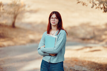 Serious girl student in glasses stands holding notebooks. Hard study, student life.