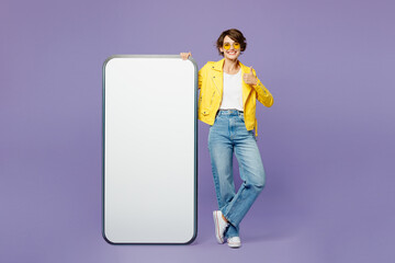 Full body young happy woman she wears yellow shirt white t-shirt casual clothes glasses big huge blank screen mobile cell phone smartphone with area show thumb up isolated on plain purple background.