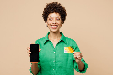 Young woman wear green shirt casual clothes using blank screen mobile cell phone hold credit bank card shopping online order delivery booking tour isolated on plain beige background Lifestyle concept