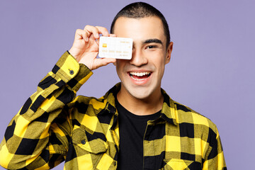 Close up young smiling middle eastern man wears yellow shirt casual clothes hold cover eye face with mock up of credit bank card isolated on plain pastel purple background studio. Lifestyle concept.
