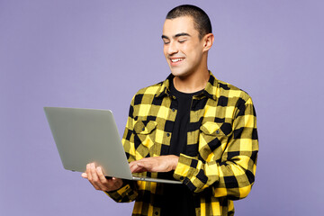 Young smiling happy smart IT middle eastern man wear yellow shirt casual clothes hold use work on laptop pc computer isolated on plain pastel light purple background studio portrait Lifestyle concept