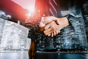 Double exposure image of business people handshake on city office building in background show partnership success of business deal. Concept of corporate teamwork, trust partner and work agreement. uds