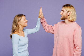 Side view young smiling happy fun couple two friends family man woman wearing pink blue casual clothes together give high five gesture isolated on pastel plain light purple background studio portrait.