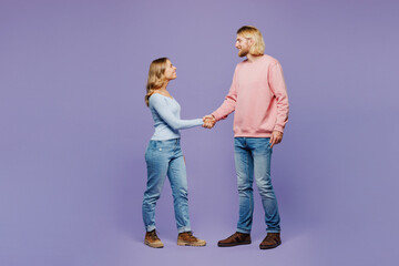 Full body side profile view young happy couple two friends family man woman wearing pink blue casual clothes together do hand shake gesture greet each other isolated on pastel plain purple background.